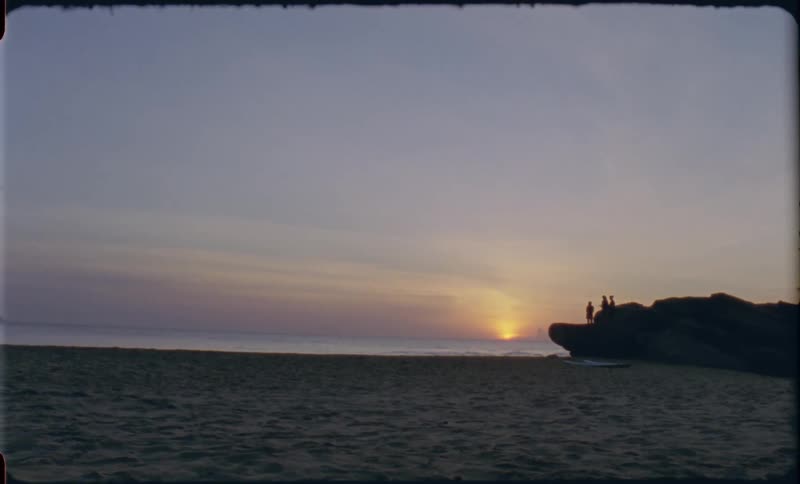 Silhouette of people stand on a big rock and watch sunset on the beach