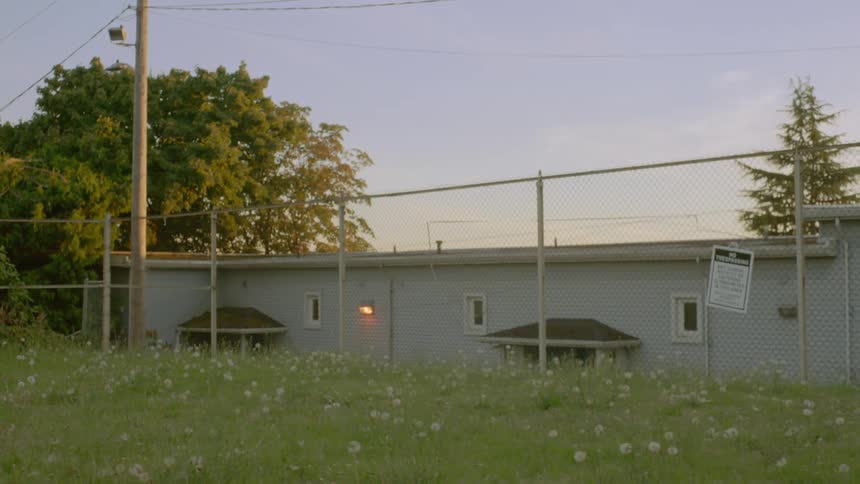 A grassy field with a fence and a house in the background