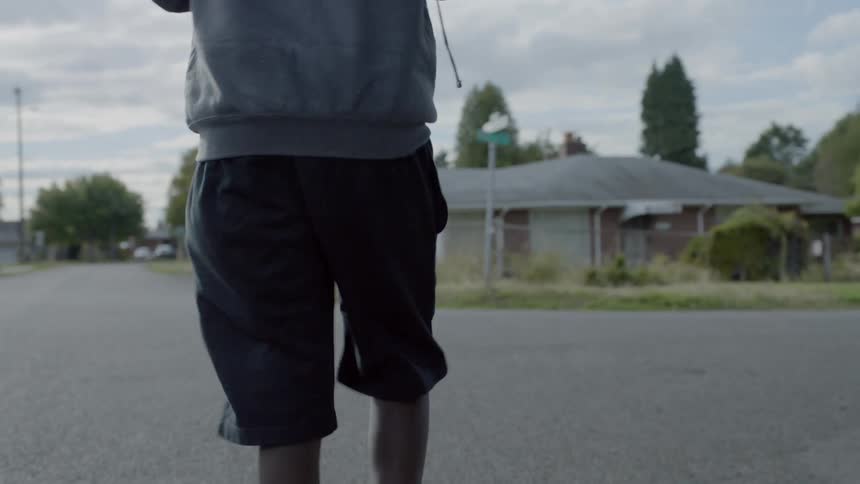 Male youth walks into the middle of the street picks up a football and turns around and walks back towards the house