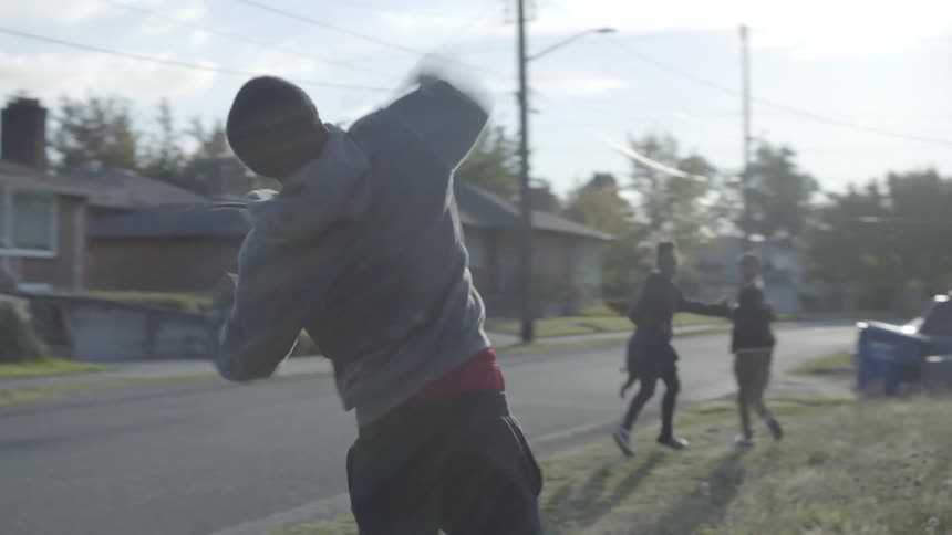 A young boy throws a football to his friends in a small yard next to a suburban road