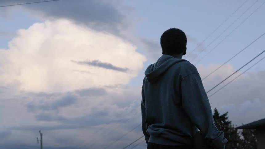 A teenage male stands outside looking at the clouds