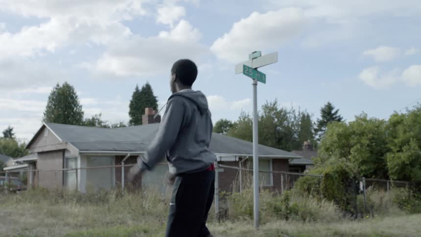 A boy walks down the street throwing a football