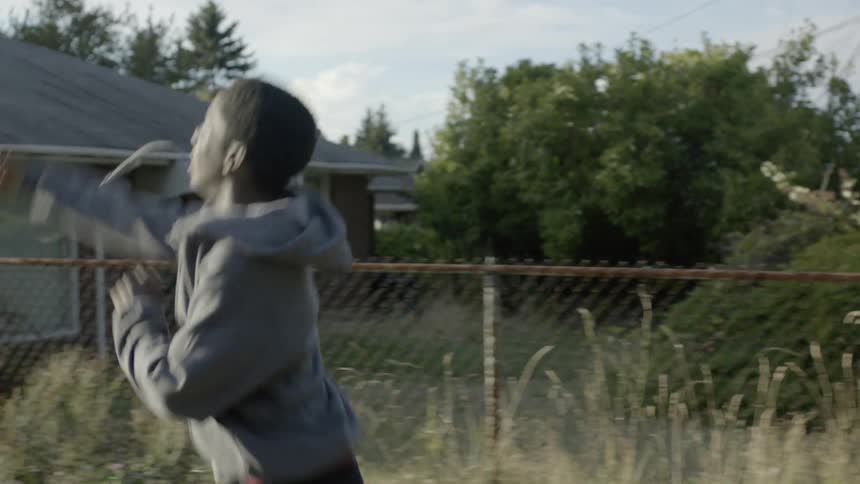 A group of kids walk down a sidewalk and then two run ahead and a boy throws a football to them