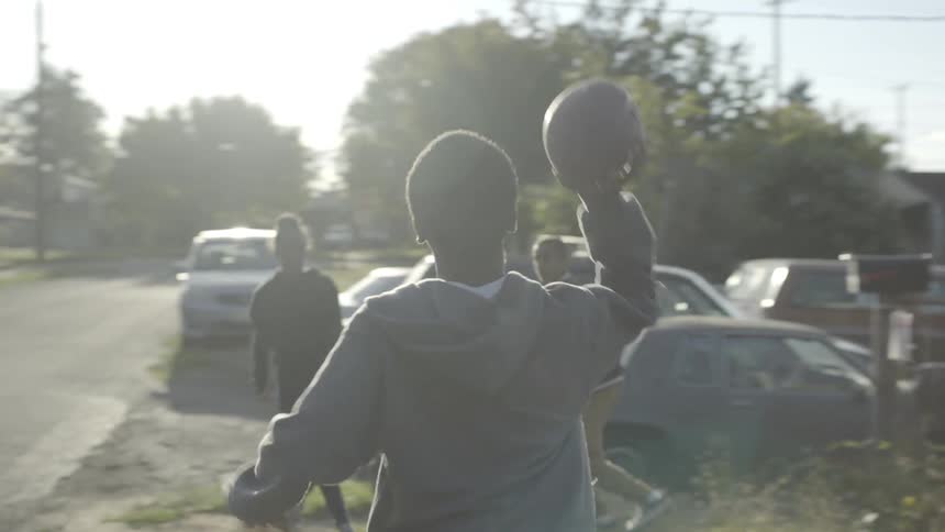Three kids play catch with a football on a neighborhood road on a sunny day