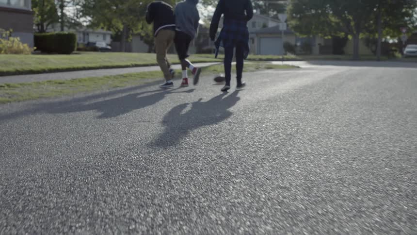 Three teenagers play with a basketball while walking on a residential street