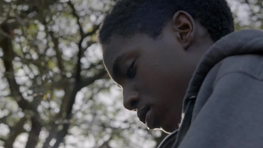 A young man sitting outdoors under a tree
