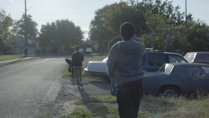 Three kids walk along a neighborhood street as they throw a football to one another