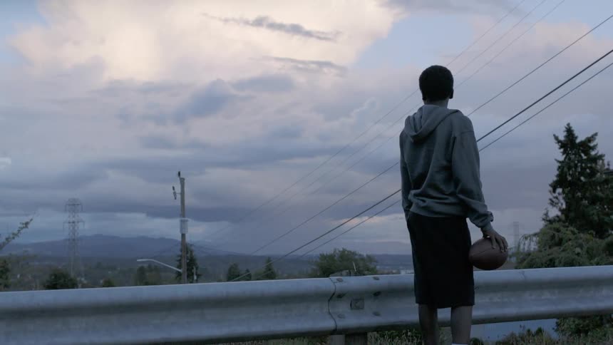 Teenager holding a football looks at the sky from a neighborhood street