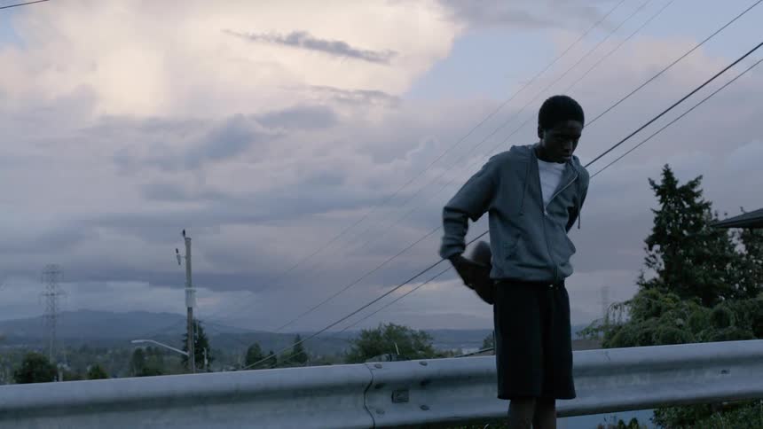 Youth plays with football standing near rail with mountain and town on horizon