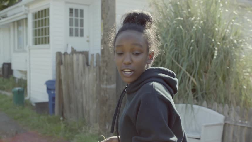A teenage girl smiles and talks while walking in a neighborhood