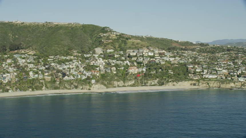 A red helicopter flies over the ocean off the coast of a small city
