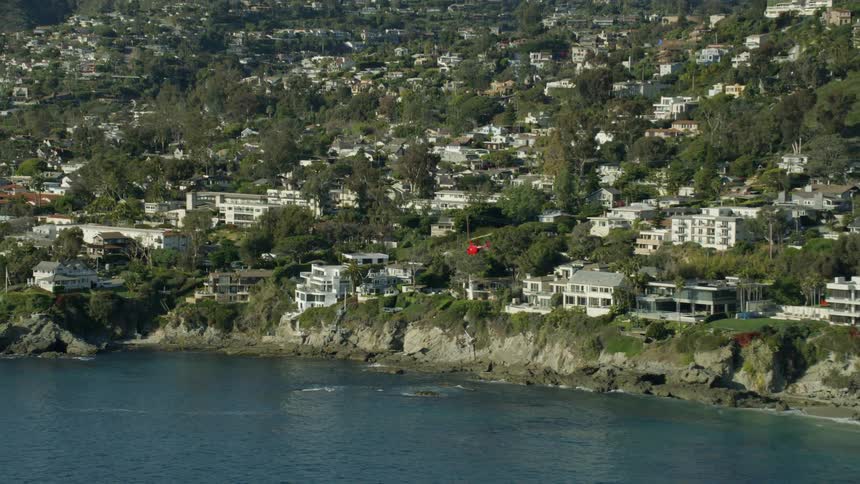 A helicopter flying over the ocean just off the coast of a city