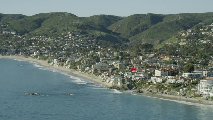 Slow motion aerial footage of a red helicopter flying by a mountain town by the coast