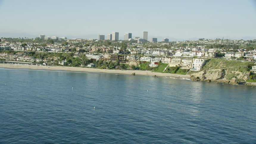 Calm ocean waves come to shore on sandy beaches below homes and neighborhoods with a city skyline on the horizon