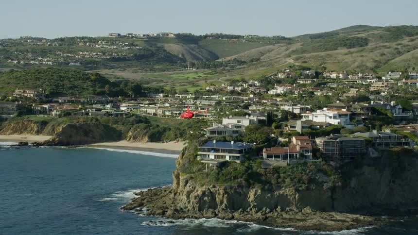Aerial reveal of helicopter flying over rugged coastline with mansions