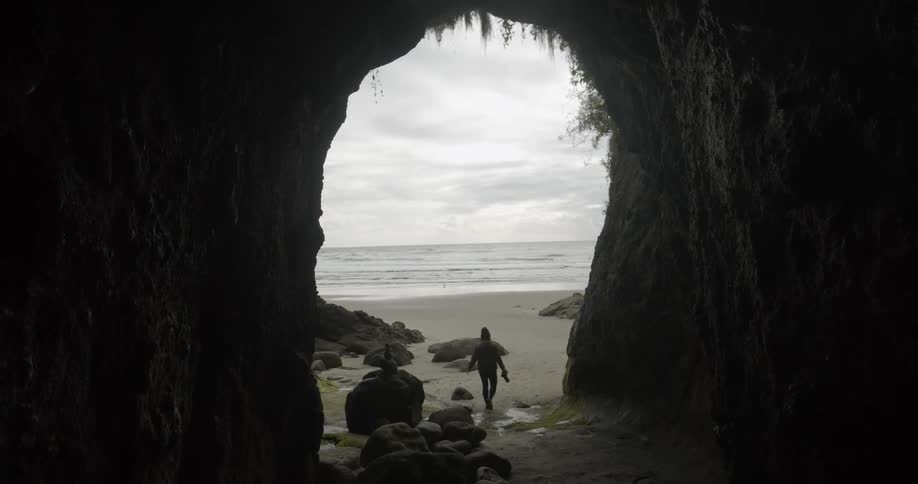 Woman walks out of the cave to the beach on a cloudy day