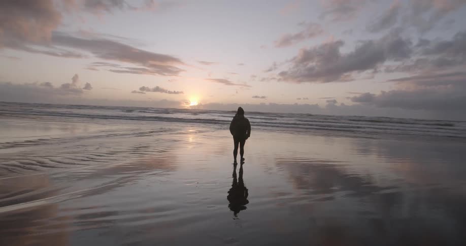 A person walks on a beach at sunrise on a cloudy morning