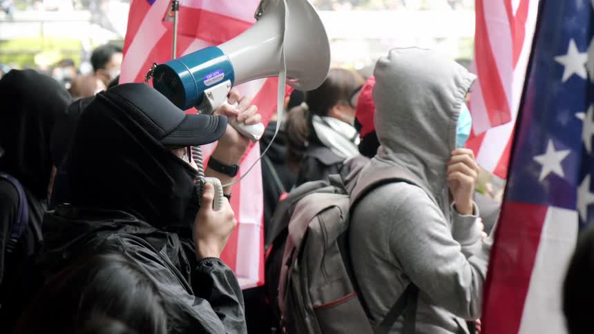 A man is speaking into a bullhorn as he stands in a crowd of people