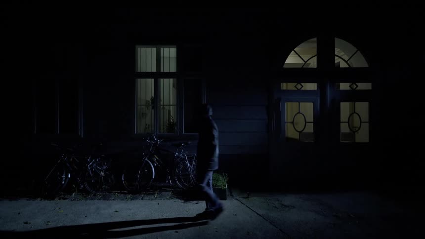 Man walks by some bicycles near a building at night