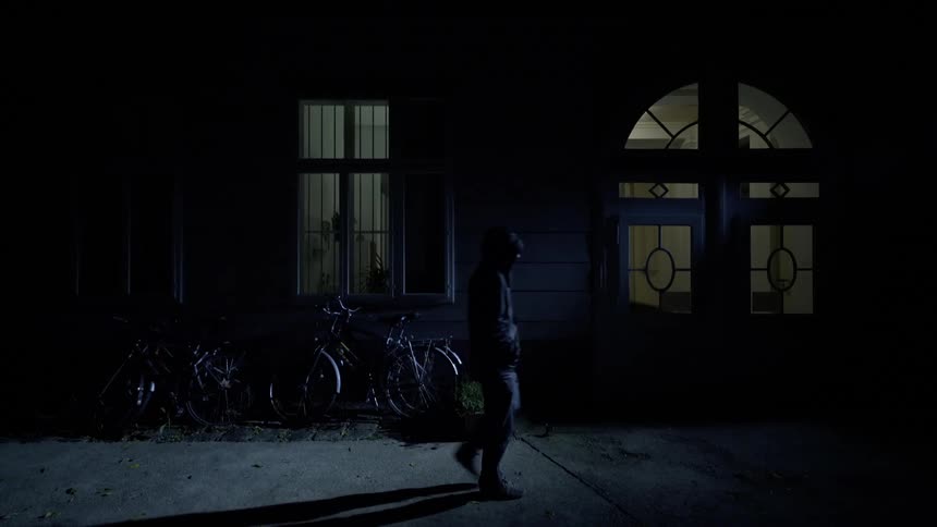 A man glances into the door of a house as he walks past at night