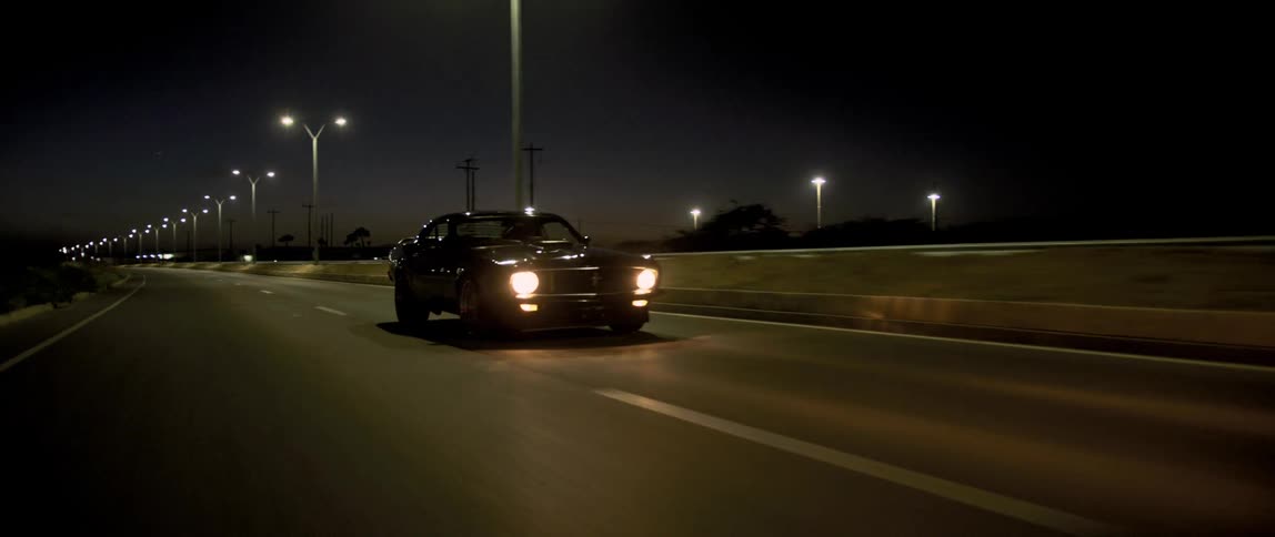 A luxury car drives on the highway past the camera at night