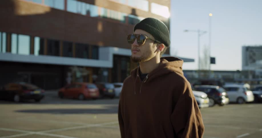 A man in sunglasses walking through the parking lot of a large building