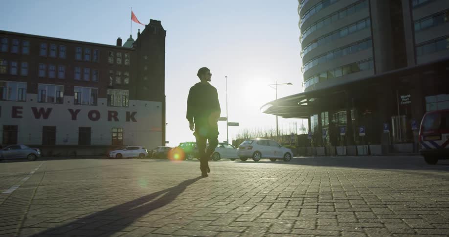 A man walking in a parking lot with a building with the word new york in the background
