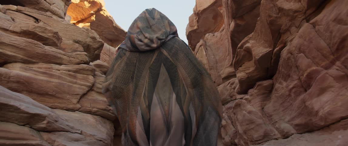 A woman with a cloak walking between a canyon