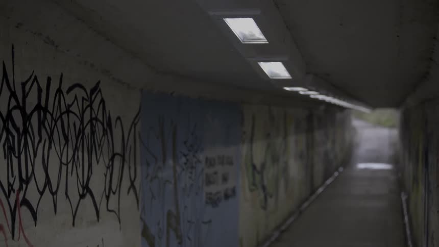 A long hall with lights in the ceiling has graffiti on the walls