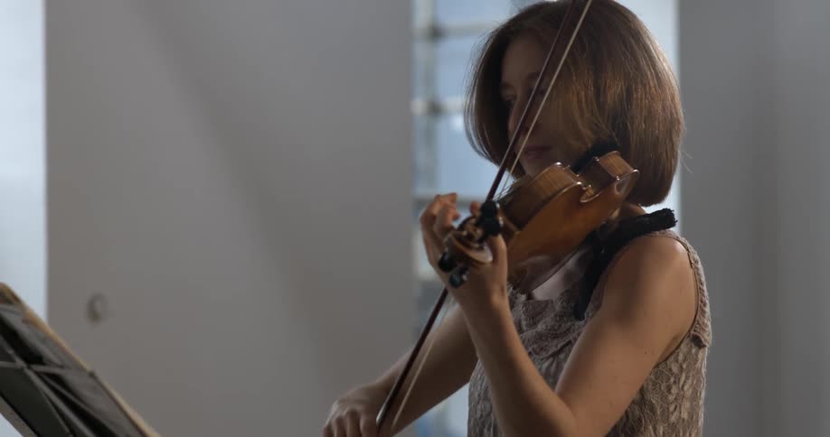 A woman plays the violin while reading sheet music on a stand