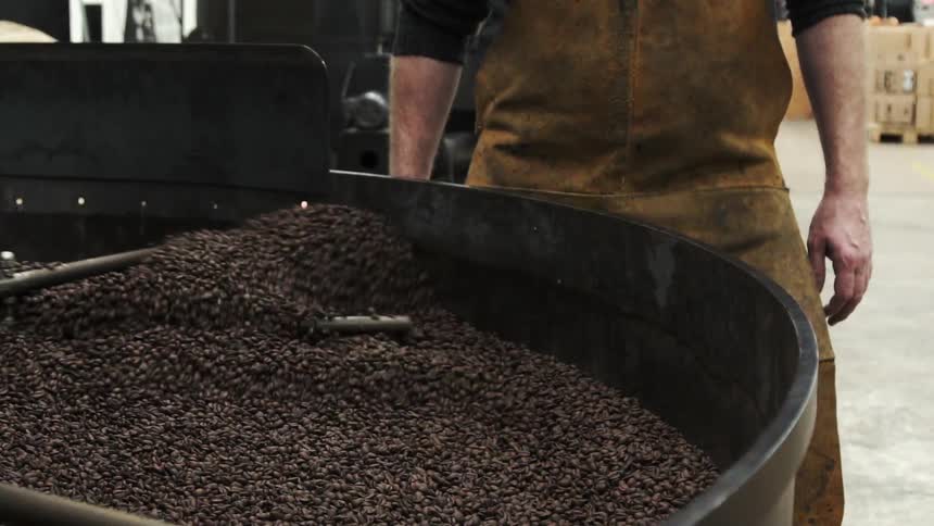 A man stands by a machine stirring beans