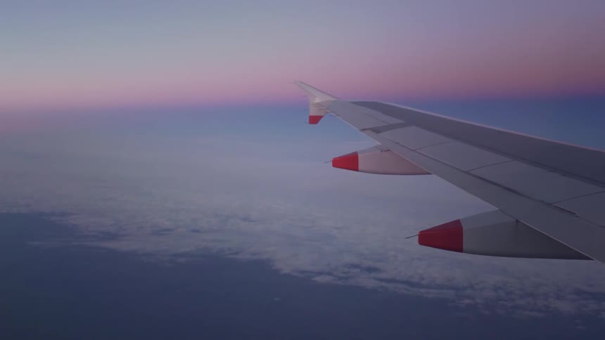The wing of a plane is seen as it flies over white clouds