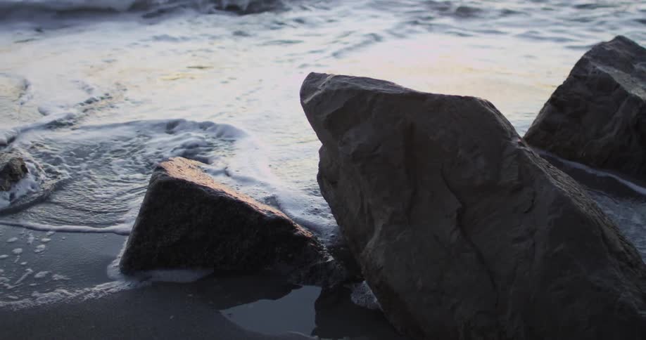 Waves come ashore beside rocks on beach