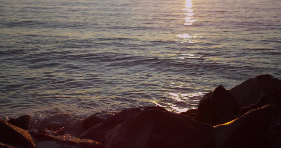 Water splashes onto rocks on the coast at sunset