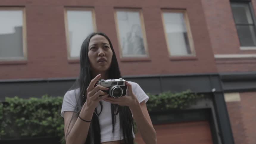 A woman is standing by a building taking photographs and talking