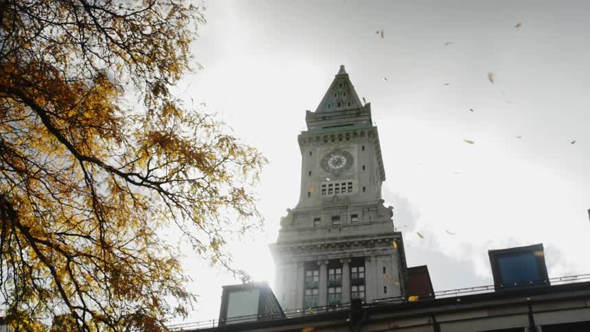 Autumn leaves fall beside a building with a tower