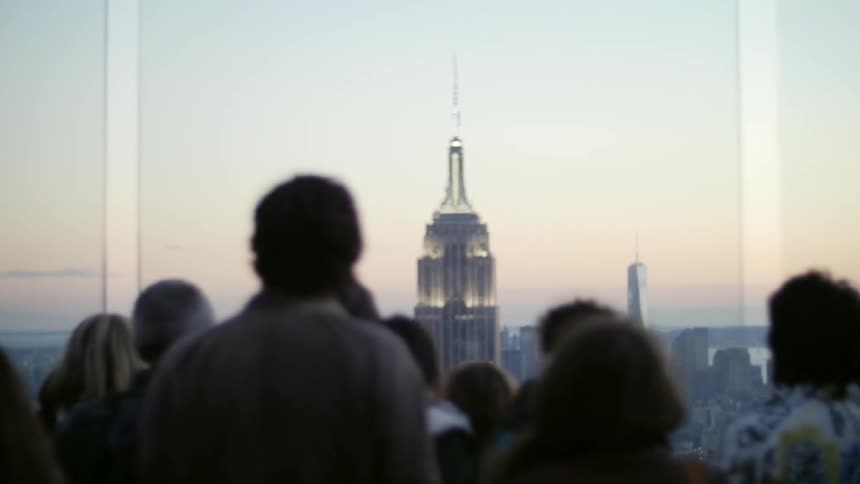 People are standing by a window looking at a tall building in the distance