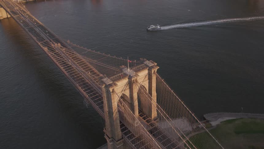 Boat leaves wake as it heads toward suspension bridge connecting city