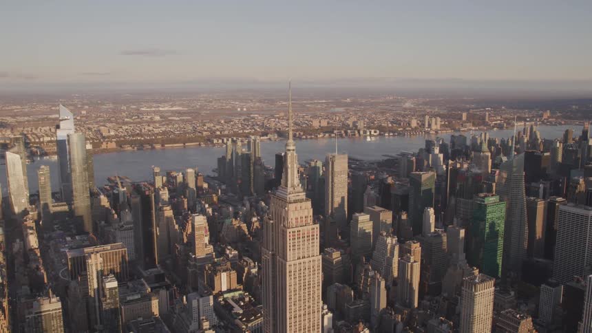 The empire state building stands tall above the other city building rooftops on a sunny day