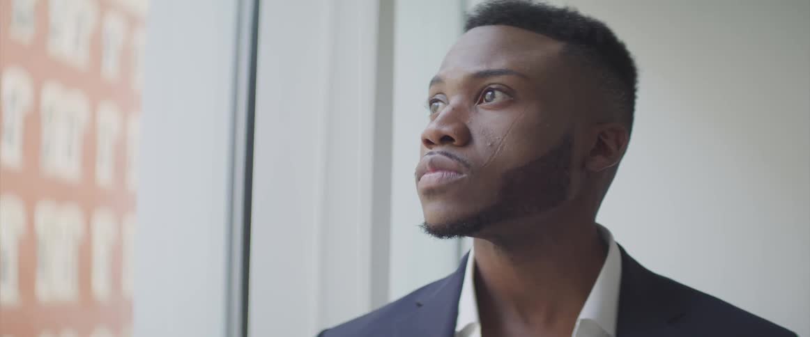 A black man lifts his head and looks out the window