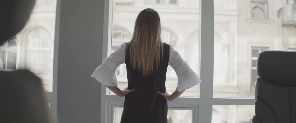 Businesswoman putting her hands on her waist and looks out the window in the office