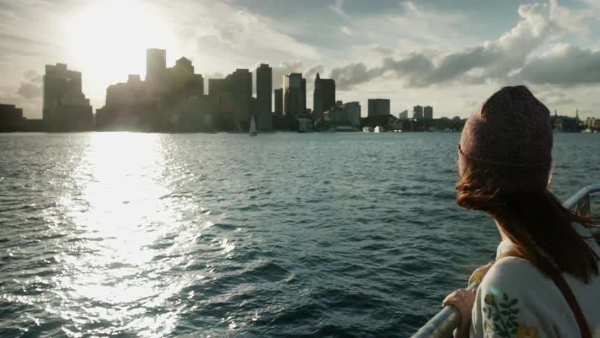 Woman stands at boat railing looking at a city skyline