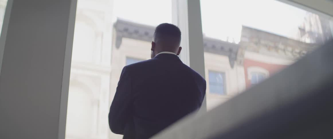 Black man stands as he looks out of a window
