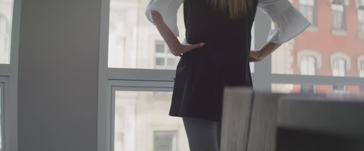 A woman puts her hands on her hips as she looks out the window