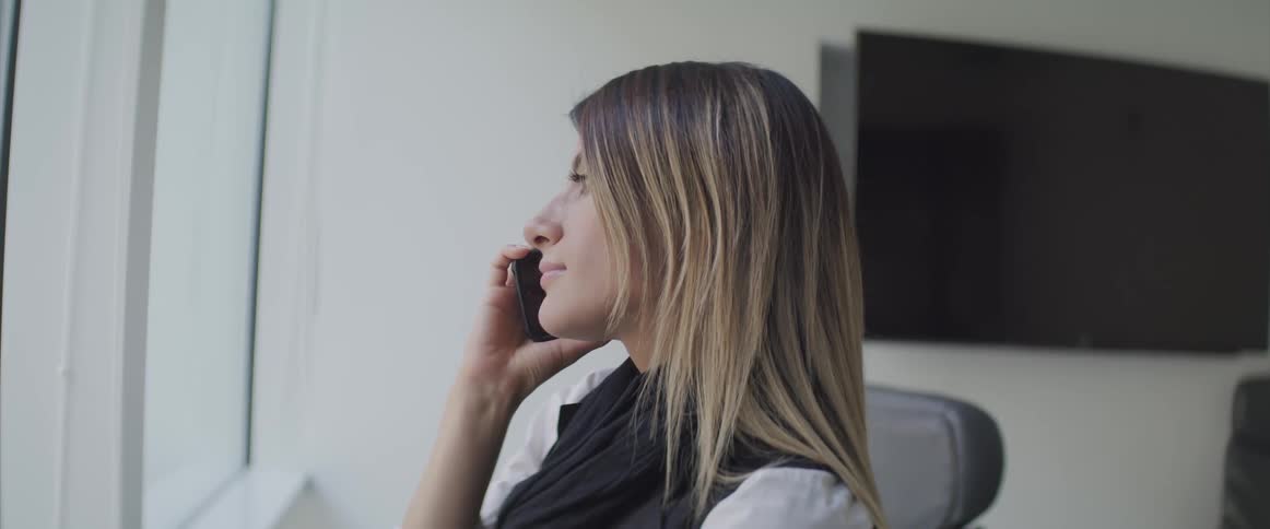 A woman looks out her office window while talking to someone on her smart phone