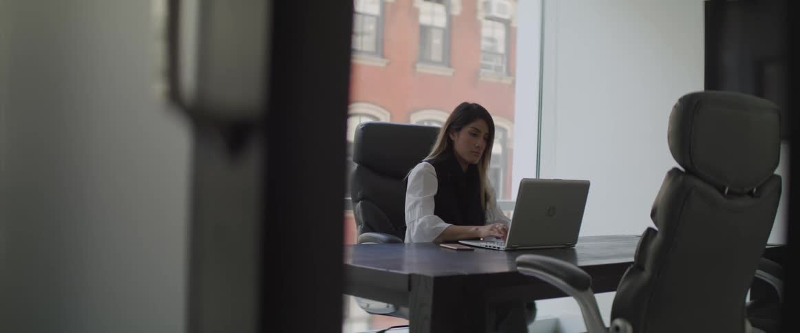 A woman sitting at a desk in an office typing on a laptop