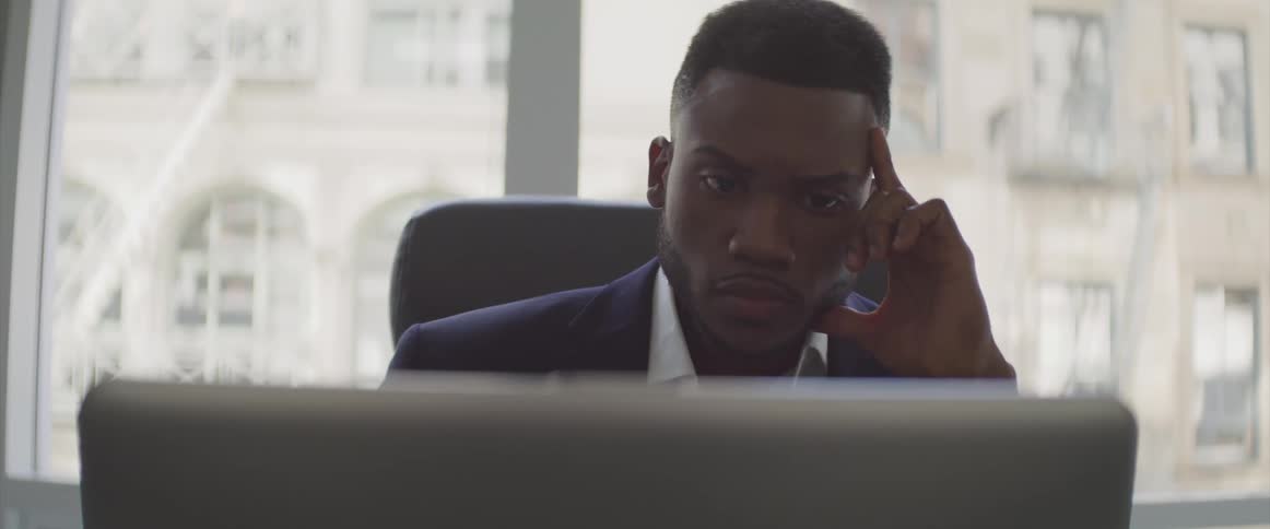 A man sits at a desk and thinks hard staring at his computer