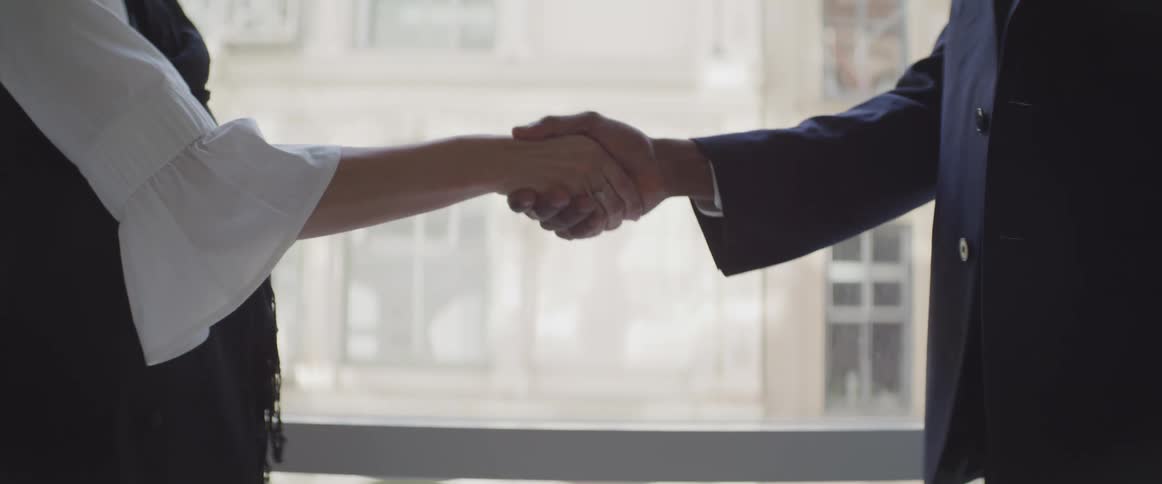 Two people shake hands in front of the window