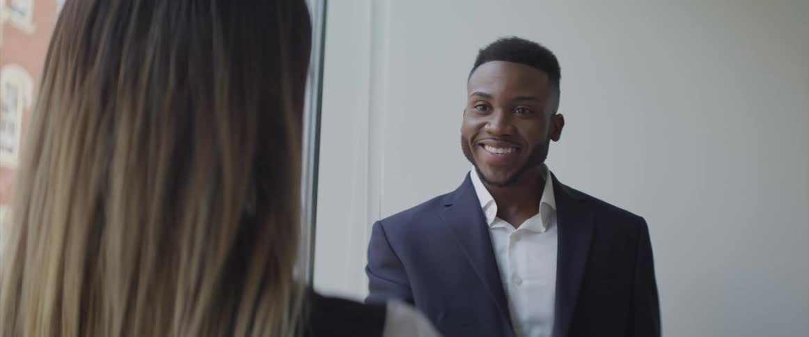 Black businessman and brunette businesswoman shake hands and smile at each other in the office