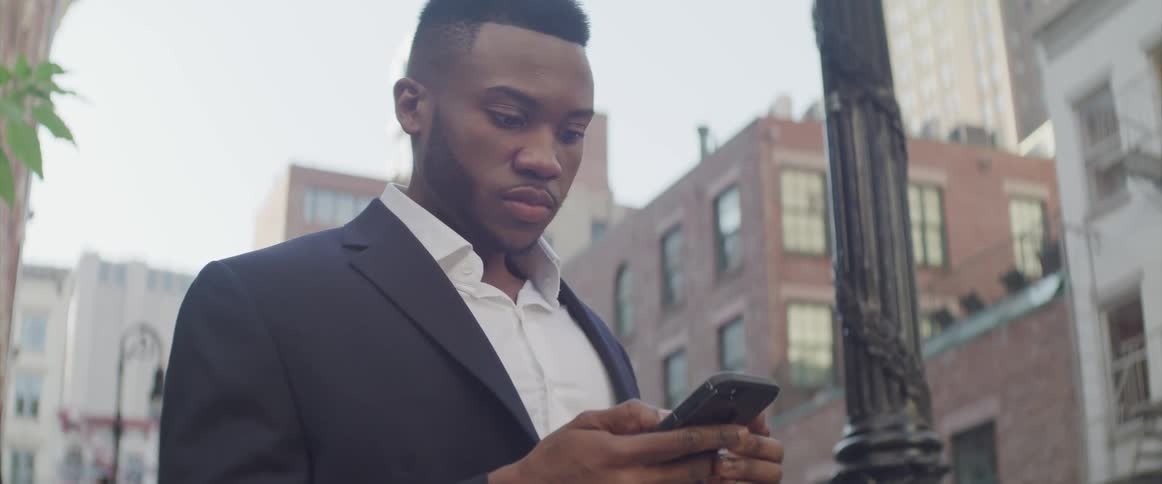 Male standing outside near a street light in front of an apartment building in the city while scrolling on his cell phone